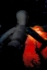 A shadowy figure carrying something -- probably a diskos -- and moving through a dark land, with patches of red glare.